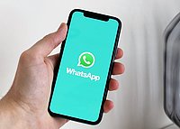 Person hält ein Mobiltelefon in der Hand, auf dem die Benutzeroberfläche von WhatsApp zu sehen ist